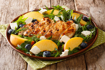 Grilled chicken breast served with peaches, blueberries, arugula and cheese close-up on a plate....