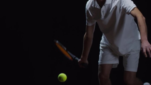Studio shot with mid-section of unrecognizable male tennis player training against black background: he hitting ball with racquet, then running after it