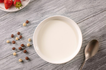 Cereal balls, a plate plate of milk and a strawberry on a gray wooden table. Top view