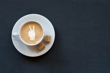 Cup of coffee with milk, cane sugar and victory sign on dark background. Top view. Copy space