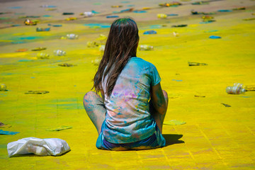 Girl decorated with colorful colors on a Hindi holiday sits on the road strewn with rubbish. People