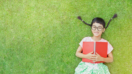 Little girl lay on grass and reading a book in a summer day