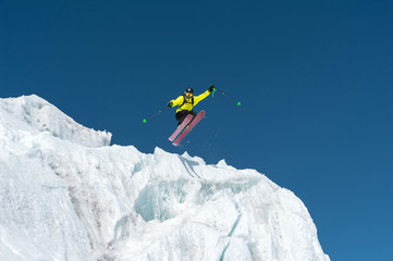 A jumping skier jumping from a glacier against a blue sky high in the mountains. Professional skiing