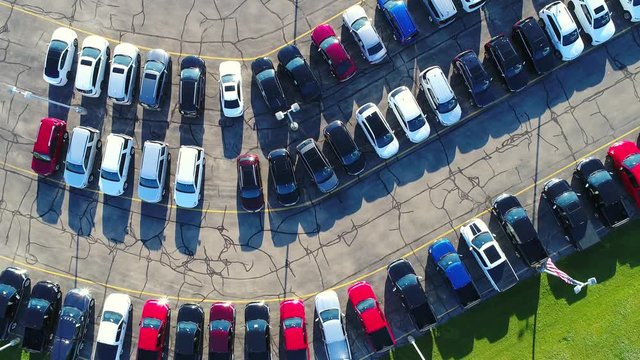 Looking straight down on new car lot, many vehicles for sale, glistening in the sun, aerial view.