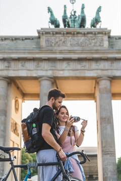 couple of tourists with backpacks and bicycle looking at photo camera in front of Brandenburg Gate, Berlin, Germany