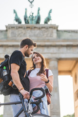 low angle view of woman talking to boyfriend with bicycle in front of Brandenburg Gate in Berlin, Germany - obrazy, fototapety, plakaty