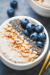 Smoothie bowl with banana, chia seeds, fresh blueberry and nuts over grey table.