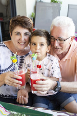 Grandparents and grandson drinking watermelon juice on the terrace in summer