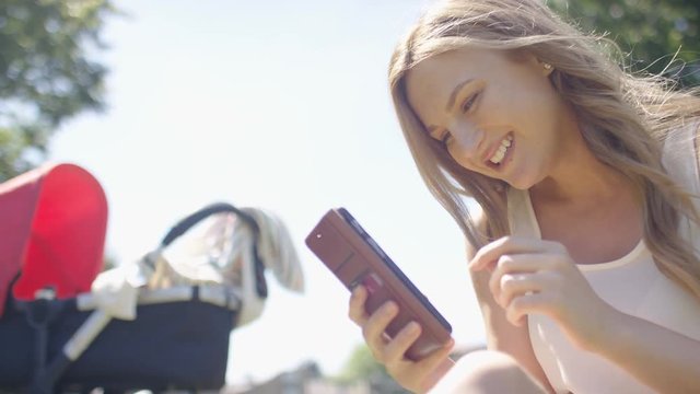 Young woman laughs as she sees something on her phone whilst outdoors in a park