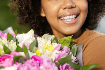 Bright smile. The close up of a beautiful young woman smiling broadly while holding pretty bouquet of flowers