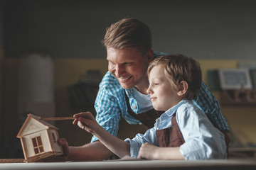 Smiling father and son with a wooden house