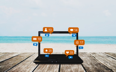 Computer laptop on wooden table at the beach in summer, with social media, social network notification icons