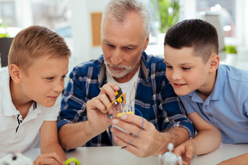 Practical lesson. Nice smart children sitting around their children while watching his working
