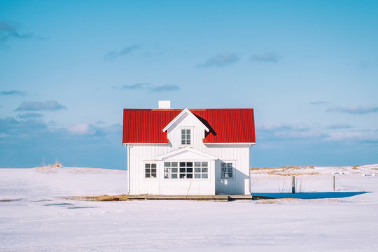 Little white house with red roof and blue sky on snowy