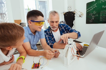Science lesson. Joyful smart teacher sitting together with his pupils while telling them about...