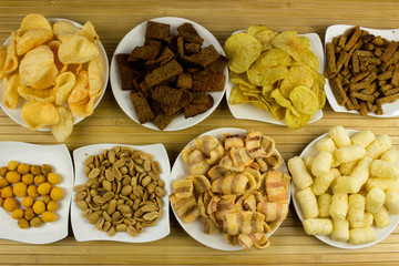 Different Snack, nut, potato chips  on a plates. Wooden table. Salty food for beer