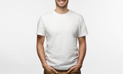 Handsome man in white tshirt isolated on grey background, smiling, standing in hands in pockets pose - obrazy, fototapety, plakaty
