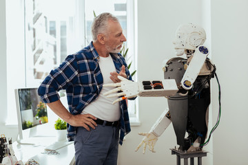 Smart technology. Serious aged man looking at the robot while having a conversation with it