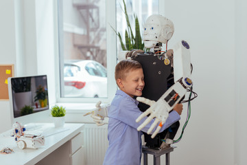 Best friend. Joyful happy boy smiling while hugging a robot