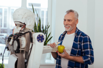 Smart technology. Cheerful nice man holding an apple while giving it to the robot