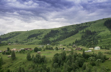 Photo of mountain village in the summer under beautiful cloudy sky. Ukraine, Carpathians, Dzembronia