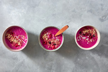 Red smoothie bowls with beets, granola, flax seeds and berries for tasty and healthy breakfast on stone background