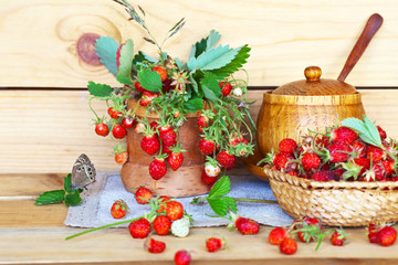 Sprigs of fresh ripe garden strawberries and berries in a wicker bowl on a wooden table on a summer day. Rustic still life