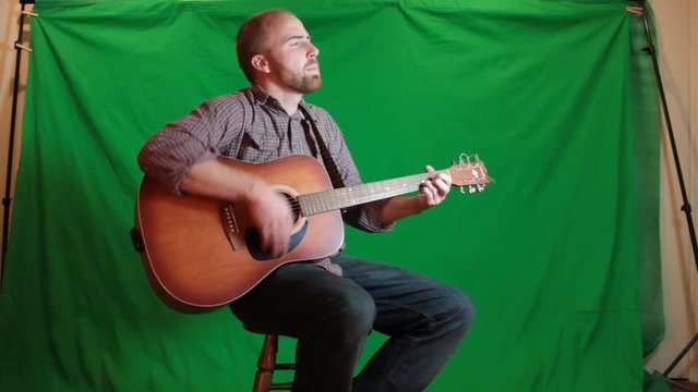 Guitar player strumming his guitar with a green screen behind him.