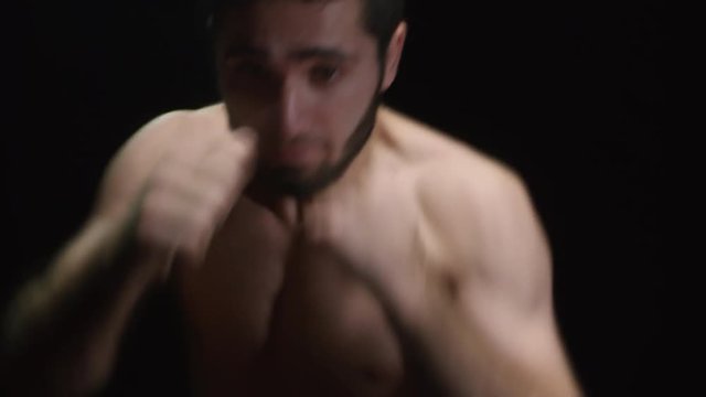 Studio shot of bearded male athlete with beard and bare chest throwing punches before camera isolated on black background