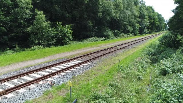 Low altitude aerial past level crossing towards railway tracks the crossing is an intersection where a railway line crosses a road or path at same level beautiful single track in forest landscape 4k