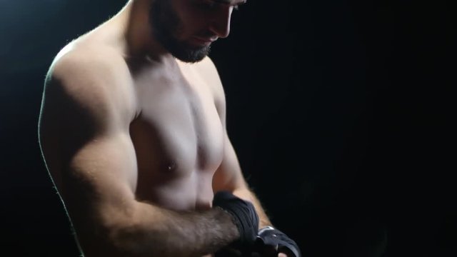 Studio shot with tilt down of focused bearded mixed martial arts fighter putting on hand wraps and preparing for fight