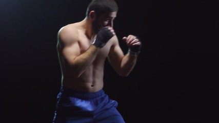 Studio shot with side view of strong male fighter in hand wraps shadowboxing against black background