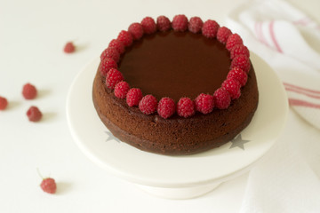 Chocolate brownie cake with raspberries and chocolate icing on a light background.