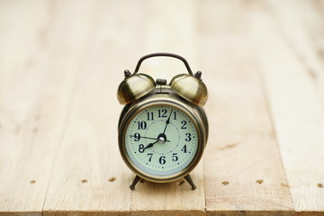 Analog alarm clock on wooden table with blur green garden background, 8 am., copy space