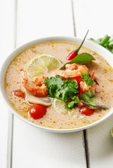Traditional thai soup tom yum with shrimps and mushrooms, served with fresh lime slices. Close up shot, white rustic wooden background.