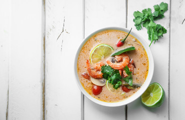 Traditional thai soup tom yum with shrimps and mushrooms, served with fresh lime slices. White rustic wooden background, copy space.