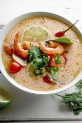 Traditional thai soup tom yum with shrimps and mushrooms, served with fresh lime slices. Close up shot, white rustic wooden background.