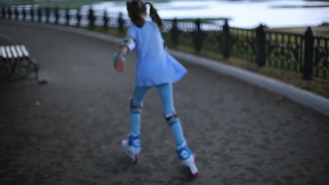 a girl in blue leggings and blue t-shirts roller skate along the promenade in the rain on a summer evening.