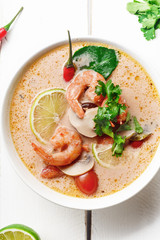 Traditional thai soup tom yum with shrimps and mushrooms, served with fresh lime slices. White rustic wooden background.