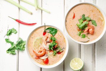 Traditional thai soup tom yum with shrimps and mushrooms, served with fresh lime slices. White rustic wooden background.