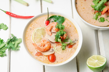 Traditional thai soup tom yum with shrimps and mushrooms, served with fresh lime slices. White rustic wooden background.