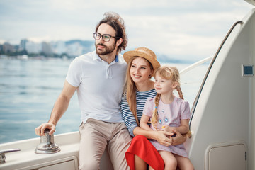 Outdoor portrait of happy family with 4-year old daughter on sailing boat at sunny summer day....