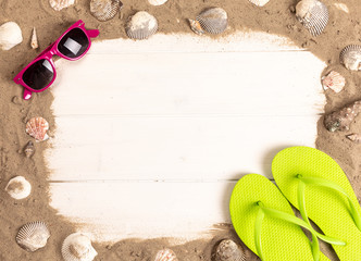frame with sunglasses, sand, shellfish and flip flops on white wooden background