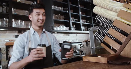 customer talking to young handsome asian barista, then taking coffee and paying with contactless credit card 4k