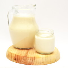 Milk carafe and yogurt jar on wooden board and white background