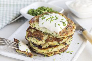 Vegetarian zucchini fritters or pancakes, served with greek yogurt and green onion on gray concrete background, horizontal
