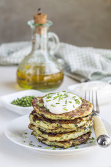 Vegetarian zucchini fritters or pancakes, served with greek yogurt and green onion on gray concrete background, vertical