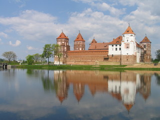 Fototapeta na wymiar Mir, Belarus. Castle Complex Mir reflected in lake On Sunny Day with blue sky Background. Old medieval Towers and walls of traditional fort from unesco world heritage list
