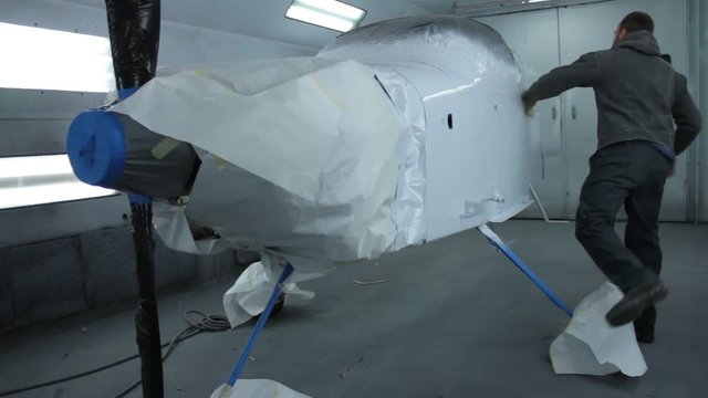 A worker uses a tack rag to prep an airplane for its next coat of paint. Plane is set up in a paint booth.