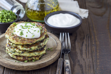 Vegetarian zucchini fritters or pancakes, served with greek yogurt and green onion on a wooden background, horizontal, copy space